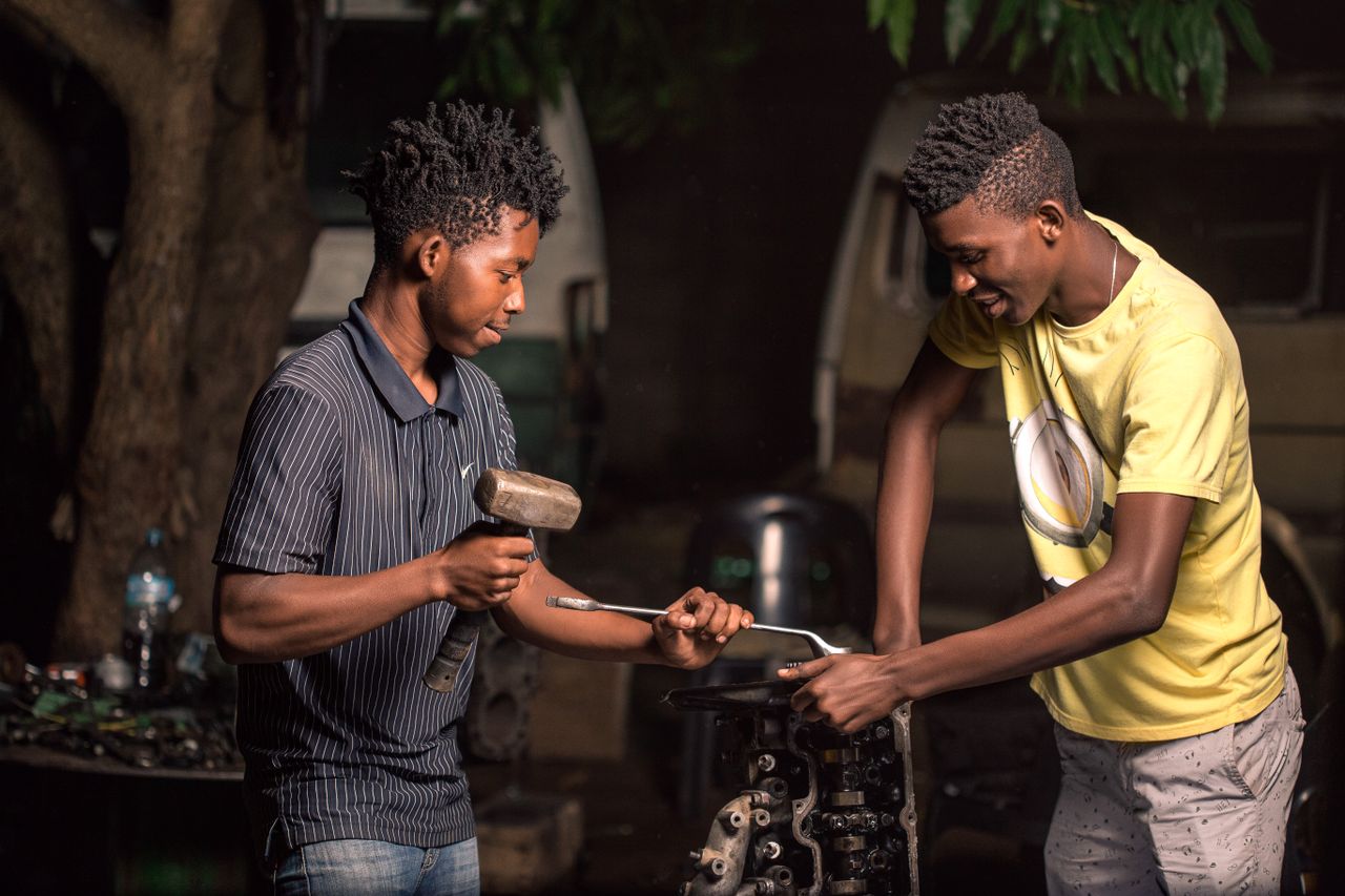 Two young mechanics working on a car engine outdoors in Mozambique.